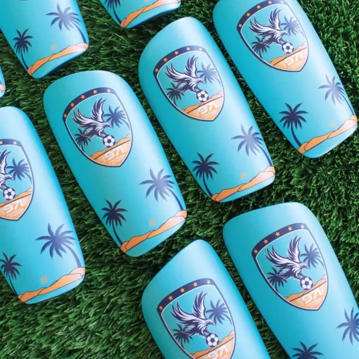 Turquoise squad shin pads with the 971 Football Academy eagle crest and palm trees