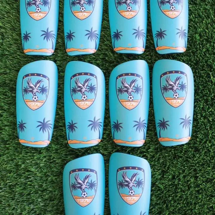 Rows of turquoise 971 Football Academy shin pads laid out on grass