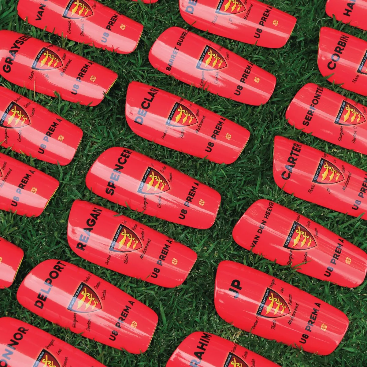 A junior squad's custom red shin pads, each with a player's name and number