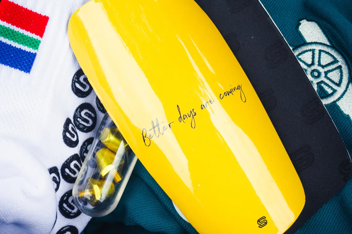 Yellow custom shin pad with a handwritten quote, next to Strapzy's grip socks