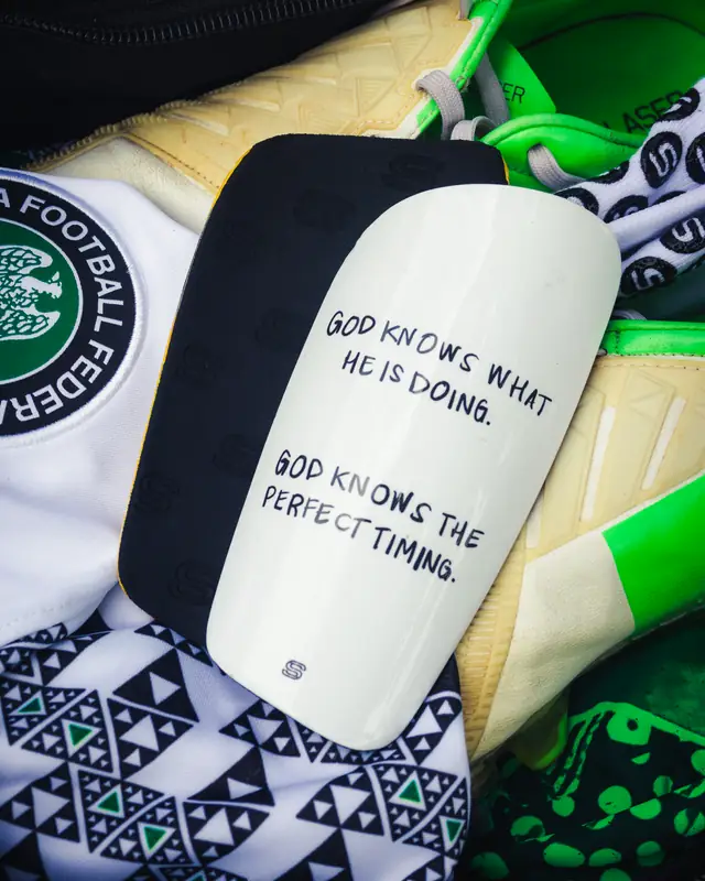 White custom shin pad with a handwritten scripture quote in a Nigeria kit
